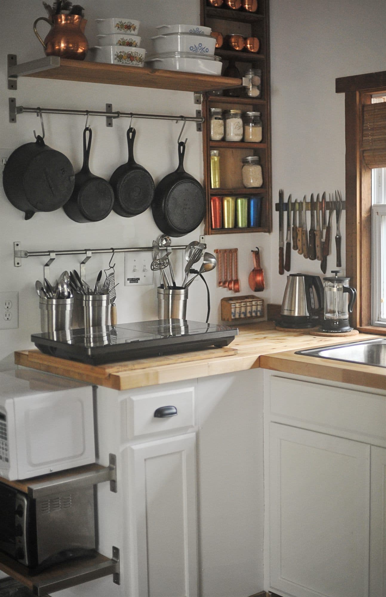 Cast iron pans hung on a rail above a butcher block counter in the cottage kitchen